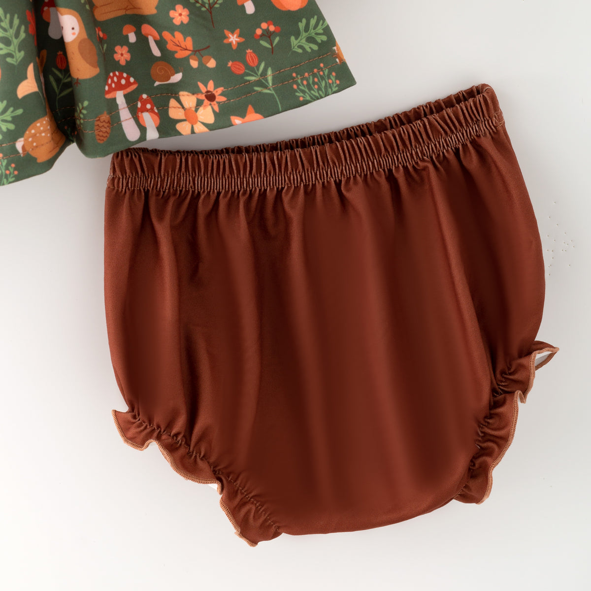 Brown baby bloomers with a green patterned top on a white background