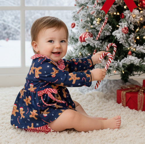 Child in a festive outfit holding candy canes in front of a decorated Christmas tree.