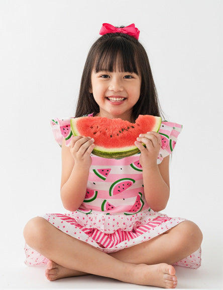 Child wearing a watermelon-themed top holding a slice of watermelon.