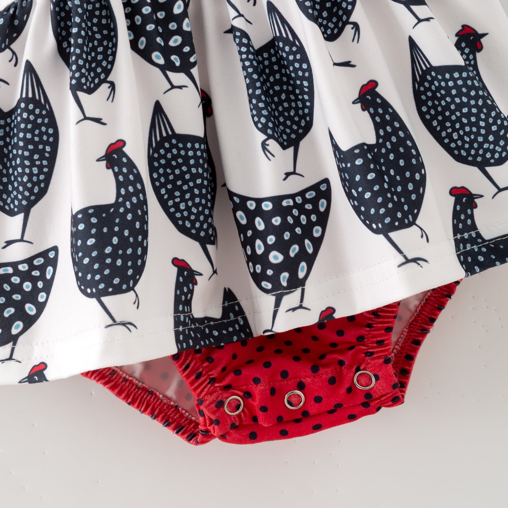 Fabric with chicken pattern and red polka dot trim on a white background