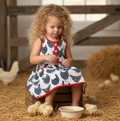 Young girl in a farm setting with chickens and hay wearing chicken print dress