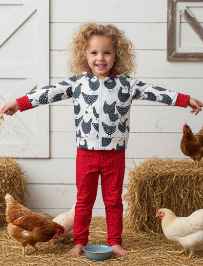 Child wearing a chicken patterned jacket and red pants standing with chickens in a barn setting
