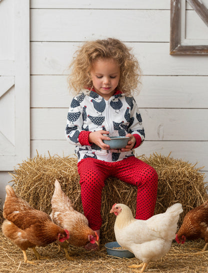 Child feeding chickens on a hay bale in front of a wooden wall.