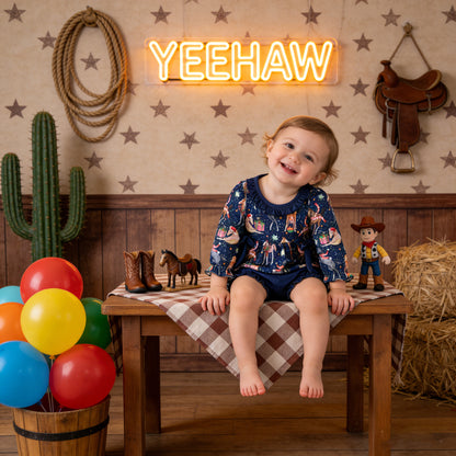 Child sitting on a table with cowboy-themed decorations and a neon 'YEEHAW' sign.