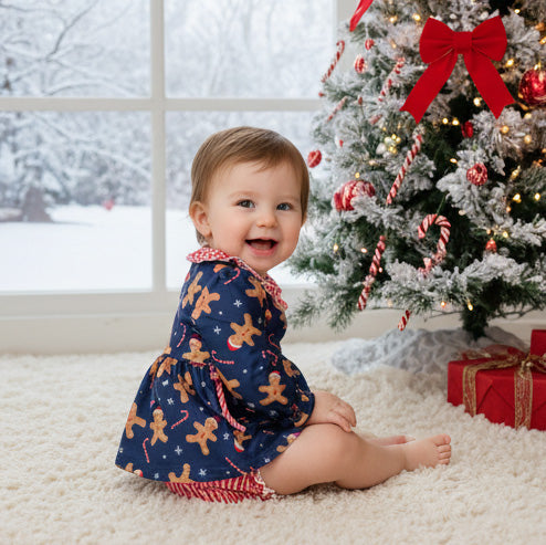 Child in a gingerbread-themed outfit sitting in front of a decorated Christmas tree.