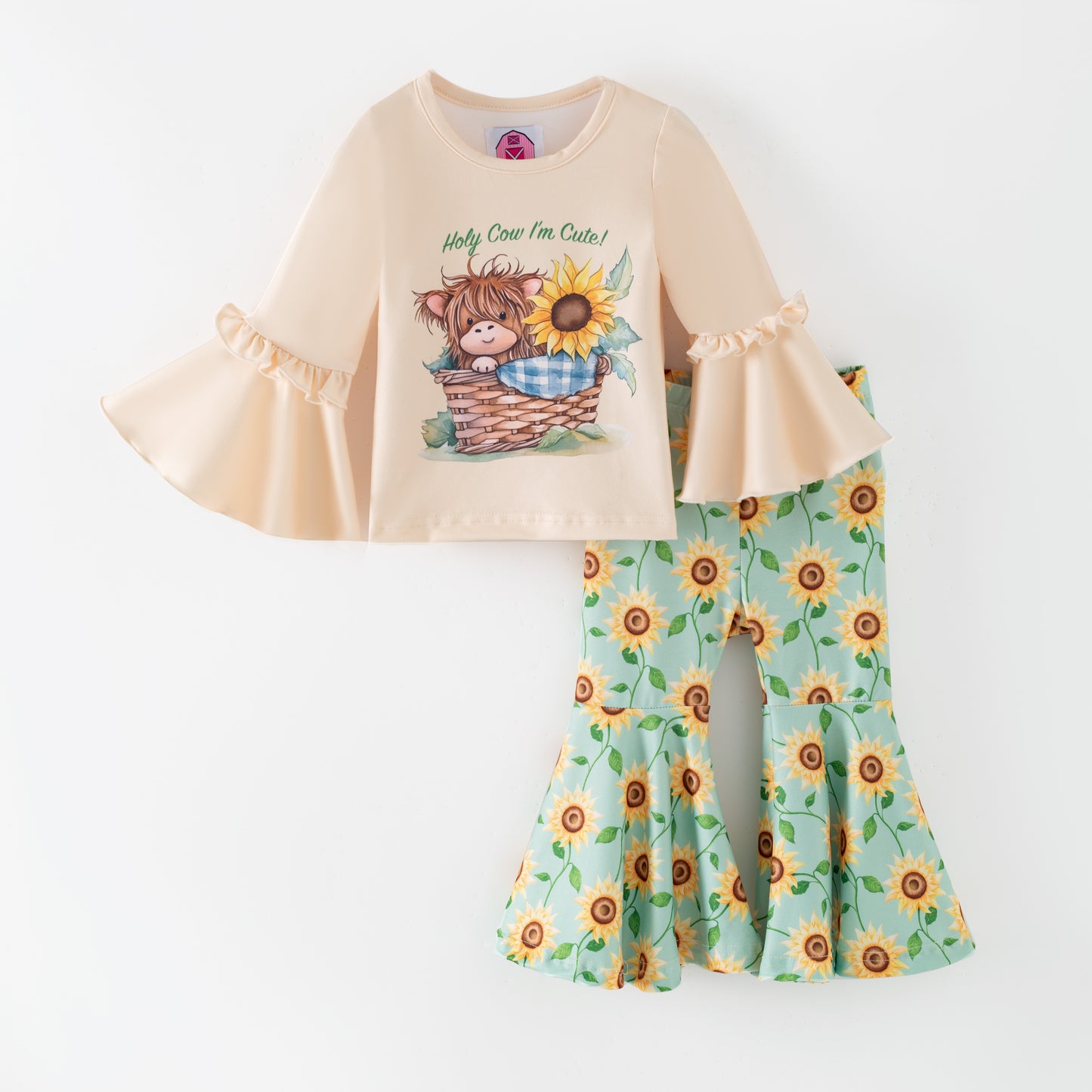 Children's outfit with beige top and sunflower-patterned pants on a green background