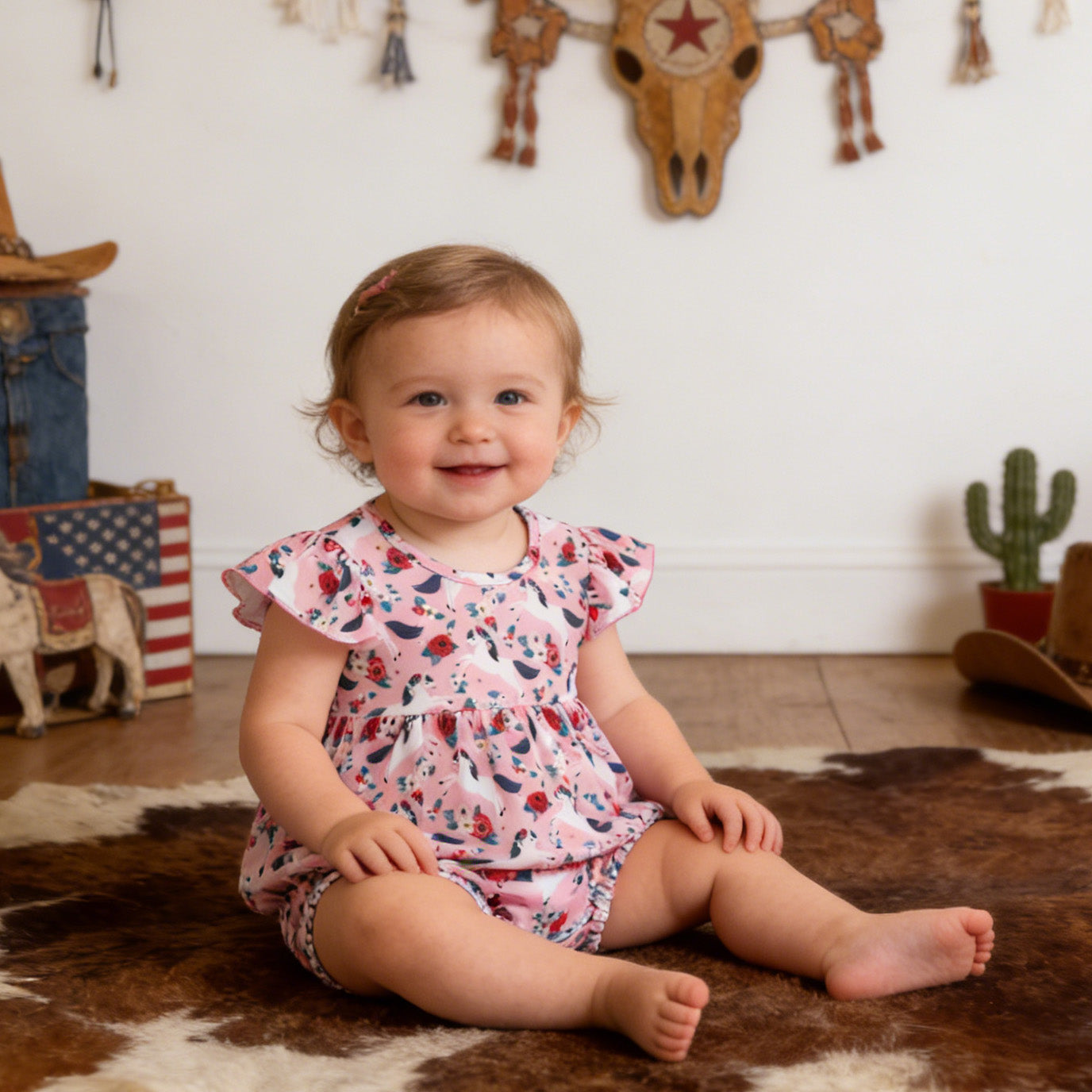 Child in a floral outfit sitting on a cowhide rug with cowboy-themed decor in the background.