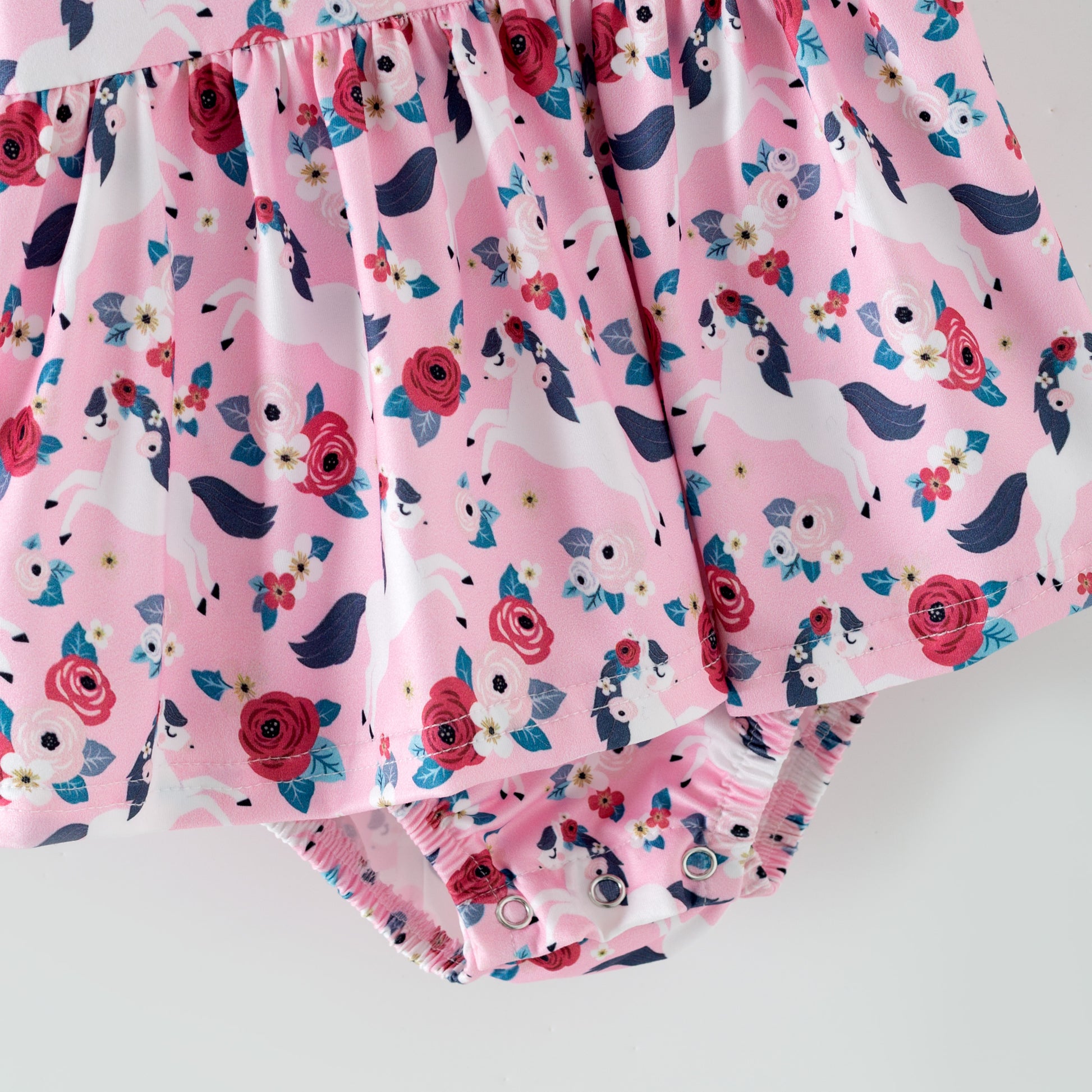 Pink floral baby romper with white horses on a pink background