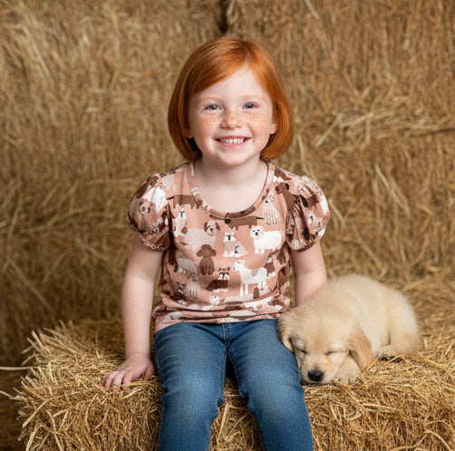 Young girl with red hair sitting on a hay bale with a puppy next to her.