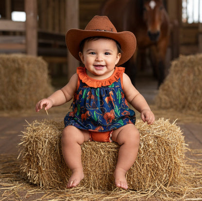 Baby in a cowboy hat sitting on a hay bale in a barn setting