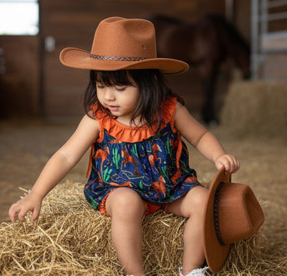 Child wearing a cowboy hat sitting on hay in a barn setting