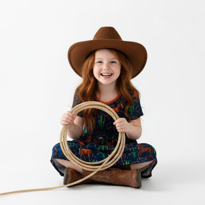 Young girl wearing a horse print patterned dress, cowboy hat, and boots on a white background