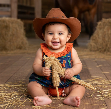 Baby in a cowboy hat and colorful outfit sitting on hay.