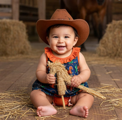 Baby in a cowboy hat and colorful outfit sitting on hay.