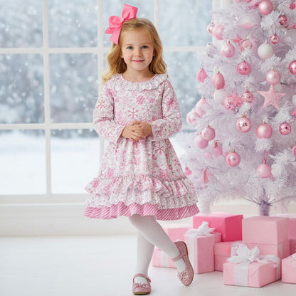 Young girl in a pink dress standing in front of a decorated Christmas tree with pink ornaments and presents.