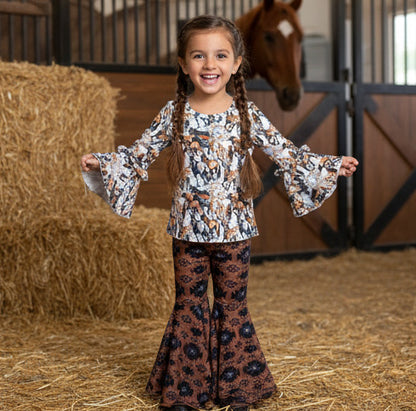 Young girl in a patterned outfit standing in a stable with a horse in the background