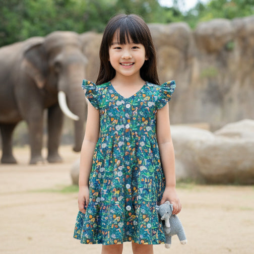 Young girl in a zoo print dress holding a stuffed animal with elephants in the background