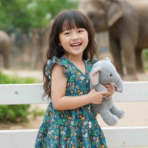 Young girl holding a stuffed elephant toy with elephants in the background