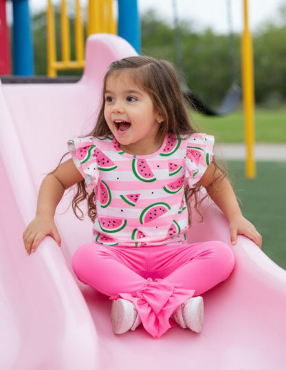 Child in a watermelon-patterned outfit sliding down a pink slide at a playground.