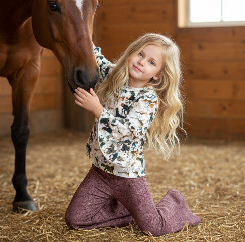 Young girl kneeling on hay with a horse in a stable