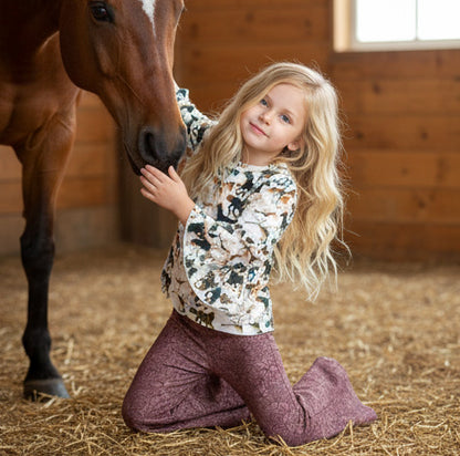 Young girl kneeling on hay with a horse in a stable