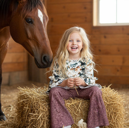 Child sitting on a hay bale next to a horse in a stable